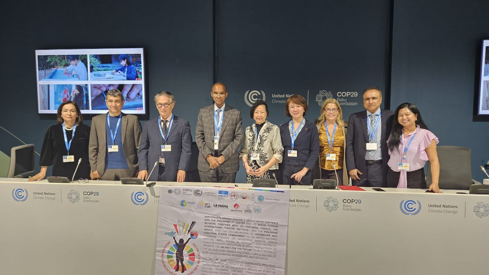 A group photo at a COP29 side event featuring panelists and distinguished guests, including Cecile Alvarez, Viktor Sebek, Ali Mohamed, and other participants. They are standing behind a conference table with COP29 and United Nations Climate Change logos, alongside a displayed resolution poster highlighting the event's themes of arts, culture, and climate action.