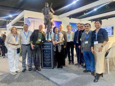 Group photo at COP29 featuring Cecile Alvarez and international delegates standing beside Jens Galschiot's sculpture 'Double Standard,' highlighting global climate justice and inequalities.