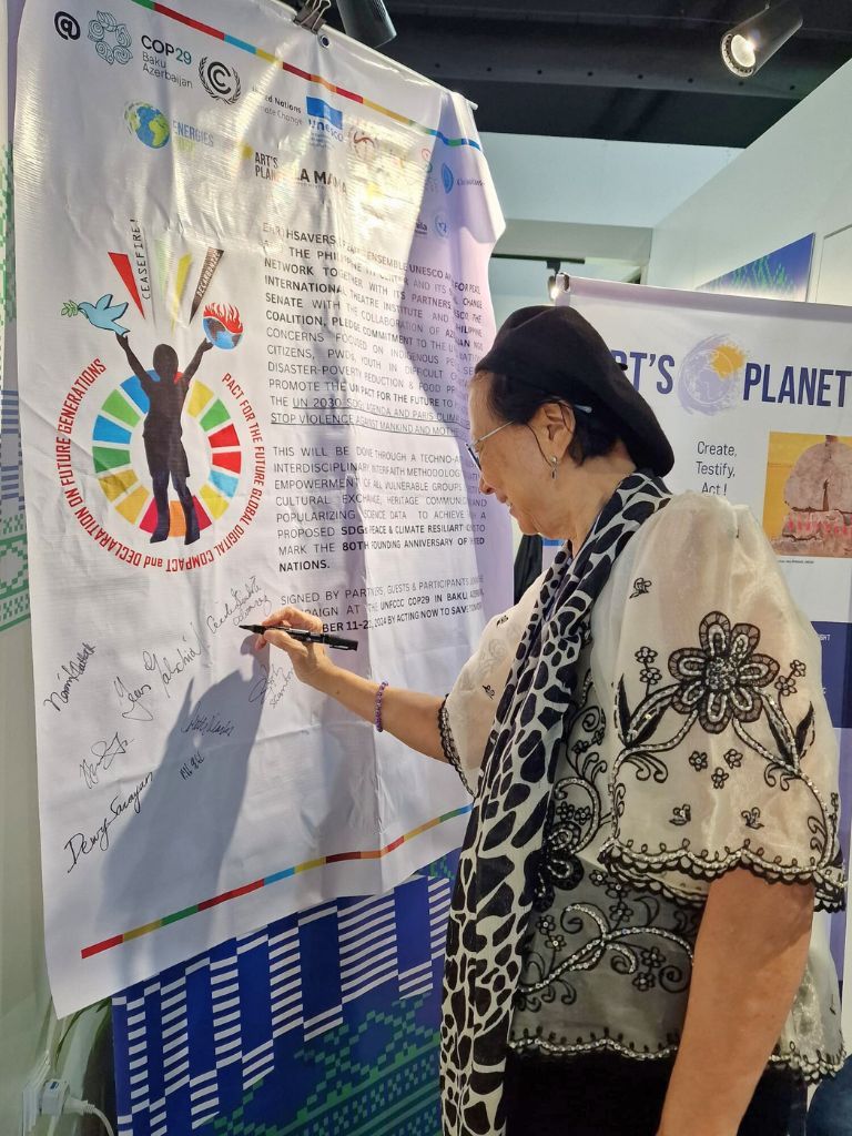 Cecile Alvarez signing a climate declaration at the Philippines Pavilion during COP29 in Baku, surrounded by banners promoting climate action and cultural diplomacy initiatives.